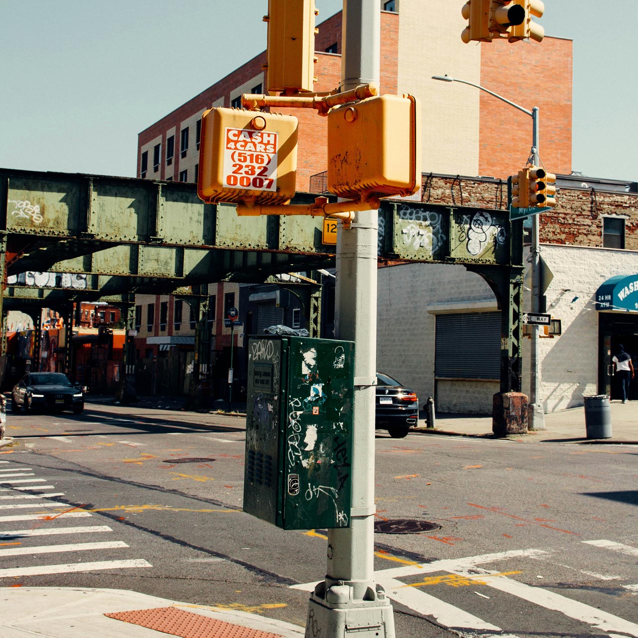 Street corner with traffic lights, sidewalk and elevated railroad viaduct in the background.