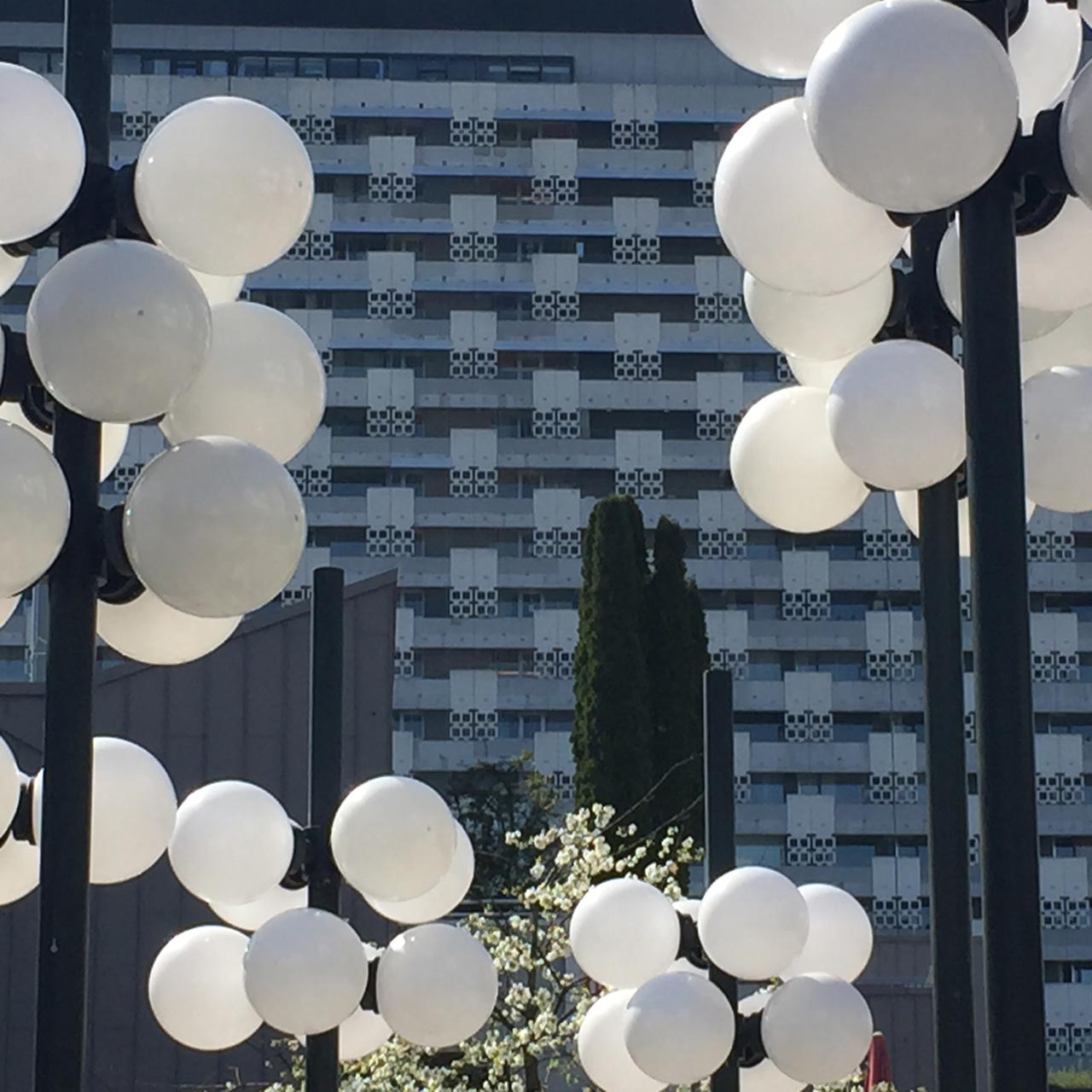 Round, white street lamps in front of a modern high-rise building with a geometric façade pattern.